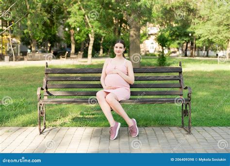 Pregnant Young Woman On Bench Sitting In The Park Pregnancy And