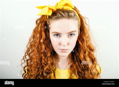 Portrait Of Curly Redhead Girl With A Yellow Bow On Her Head Wearing