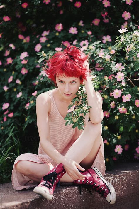 caucasian female with bright red hair sitting near a flowering briar