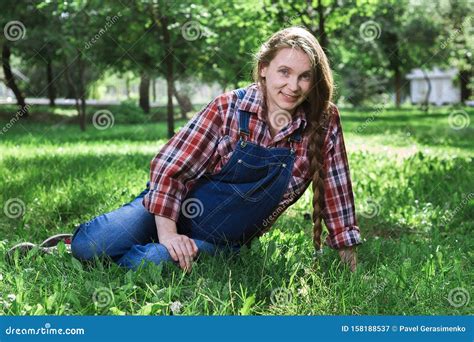 Beautiful Pregnant Woman In Denim Overalls Sitting On The Grass In The