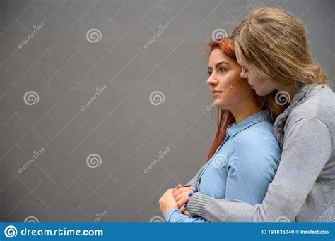 Two Happy Girlfriends Are Hugging On The Background Of A Gray Wall
