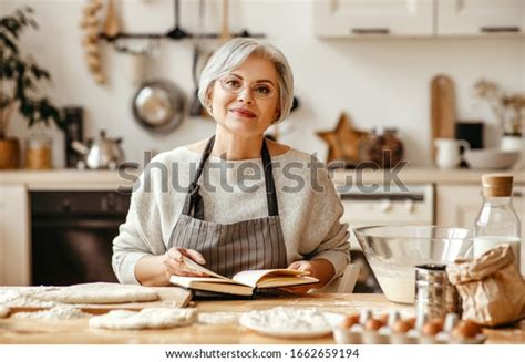 Happy Old Woman Granny Cooks In Kitchen Kneads Dough And Bakes Cookies
