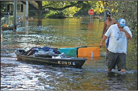 a man pulls a boat down a flooded street with some of his belongings he recovered from his home as