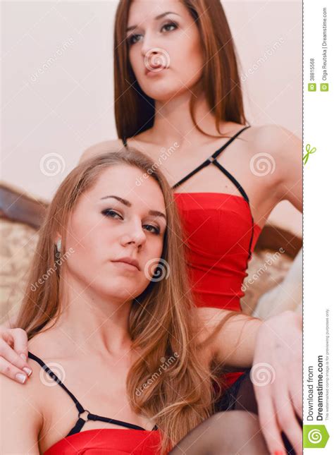 two girl friends in red dress sitting on the bed stock