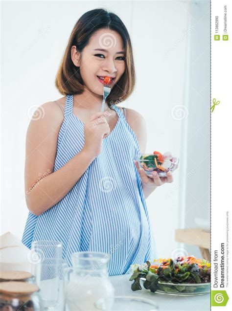 asian pregnant woman is eating salad she looks healthy because the food is beneficial stock