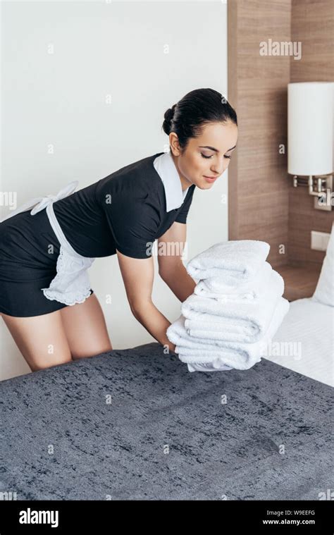 Pretty Maid In White Apron Putting Pile Of Folded Towels On Bed In