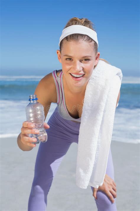 Sporty Smiling Blonde Standing On The Beach With Towel And Bottle Stock