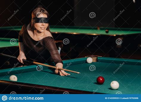 a girl with a blindfold and a cue in her hands in a billiard club