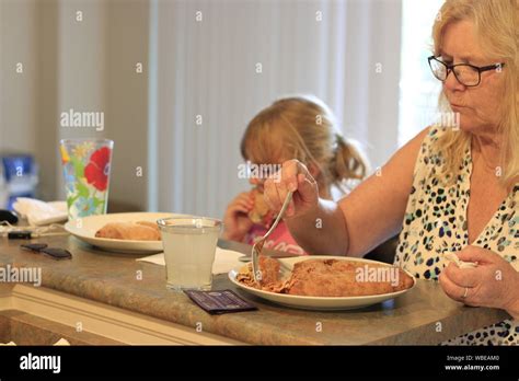 Grandma And Granddaughter Eating Dinner Together At A Kitchen Table