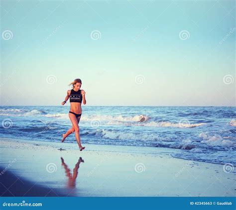 attractive female runner running along the beach at amazing sunset with