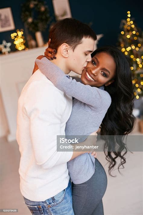 크리스마스 밤에 거실에서 껴안고 있는 아름다운 흑인 소녀와 백인 남자 인종 간 관계 사랑에 빠진 신혼 부부 새해 축하 커플에