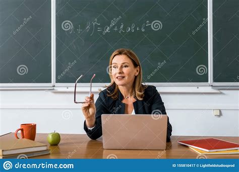 female teacher sitting at computer desk holding glasses and talking