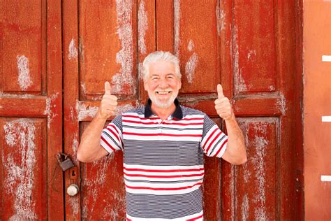 People Senior With White Beard And Hair Standing Behind An Old Red Door