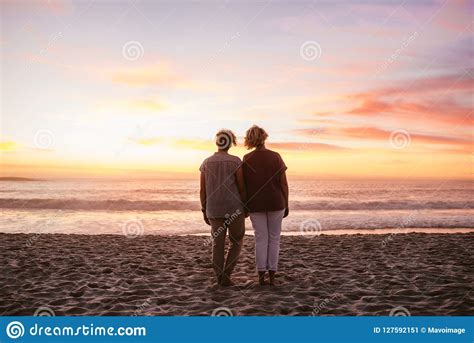 Young Lesbian Couple Standing On A Beach Watching The Sunset Stock