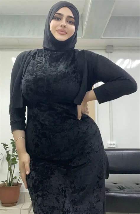 a woman in a black dress and hijab poses for the camera with her hands