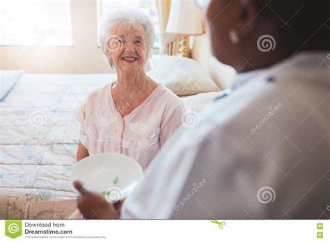Senior Woman On Bed With Nurse Giving Medication Stock