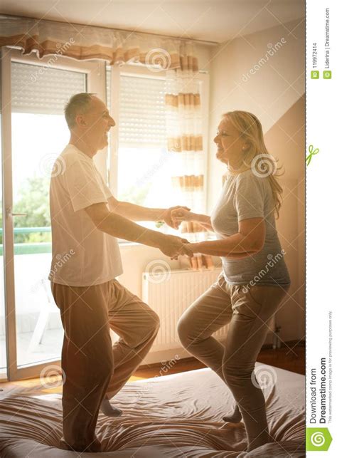 senior couple dancing and jumping together on bed holding