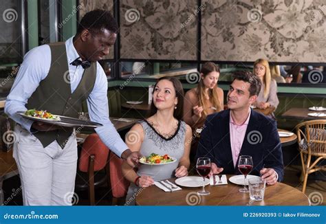 African American Waiter Serving Couple At Restaurant Stock Image