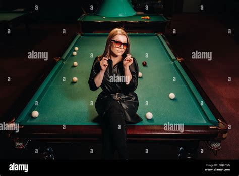 a girl with glasses sits on a pool table in a club russian billiards
