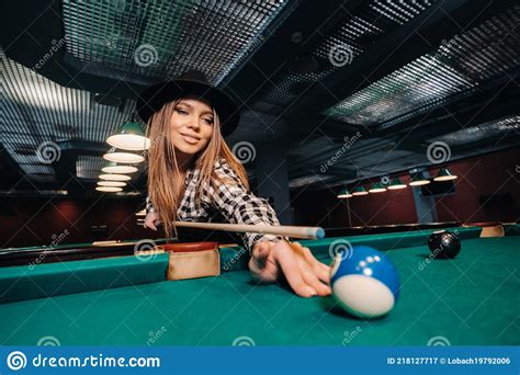 a girl in a hat in a billiard club with a cue in her hands hits a ball