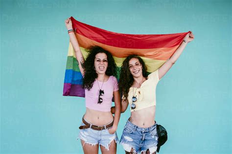 Cheerful Lesbian Couple Holding Rainbow Flag While Standing Against