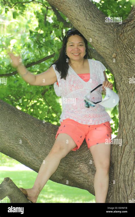 mature asian woman wearing shorts sitting on a large branch of a big