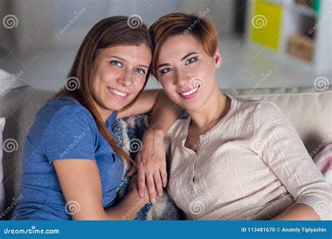 Homosexual Couple Of Lesbian Women At Home On The Couch Hugging Stock
