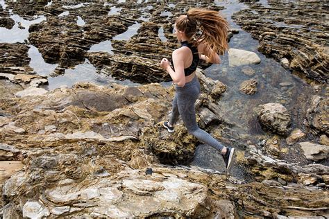 athletic female running on rocks at the beach by stocksy contributor