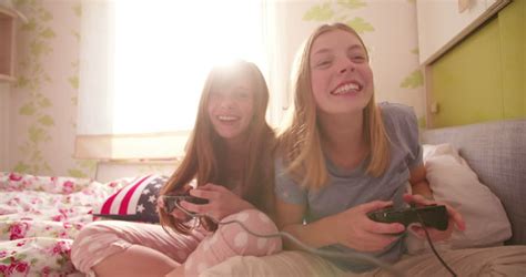 teen girl on a bed pushing her laughing friend in a joking