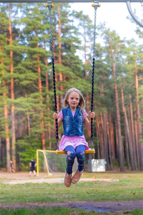 Little Blonde Girl Smiling Swinging Outdoors On A Playgroung Stock