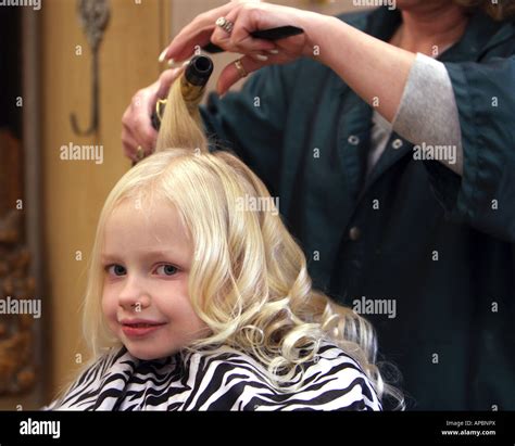 a little blond haired girl getting her hair styled in a hair salon