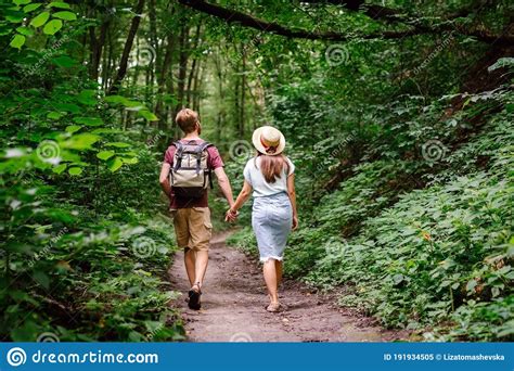 couple holding hands walking in forest back view