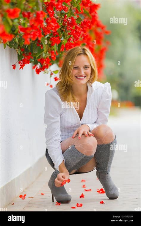 Young Woman Squatting Squat On Street Besides Red Flowers Smiling Stock
