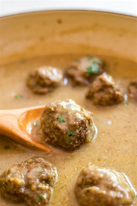 one of the classic swedish meatballs on a spoon in a pan containing other classic swedish