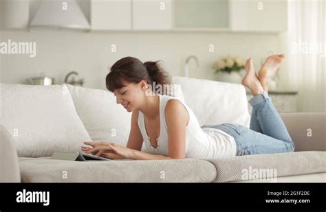 Cute Girl Lying On Sofa Using Touchpad And Smiling At Camera Stock
