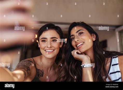 Two Women Sitting Outdoors Looking At A Mobile Phone Smiling Women