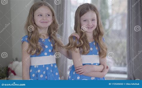 smiling brunette caucasian twin sisters in similar dotted blue dresses