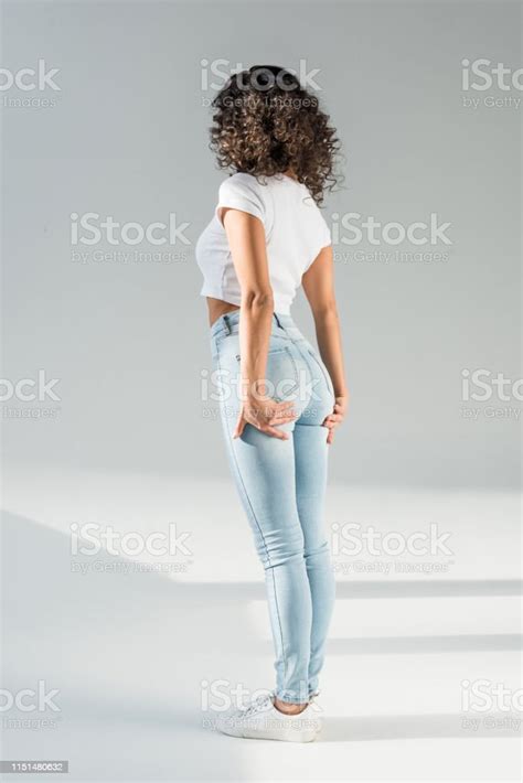 Back View Of Woman Standing In Tight Blue Jeans On Grey Background