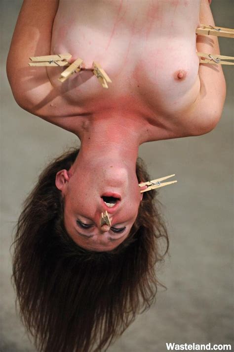 nude female is hung upside down so another woman can torture her