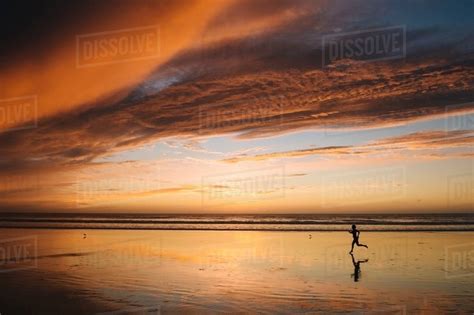 side view of mid adult nude womans silhouette running on beach under