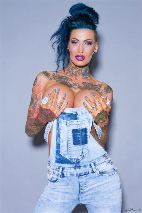 a woman with blue hair and tattoos on her chest wearing overalls