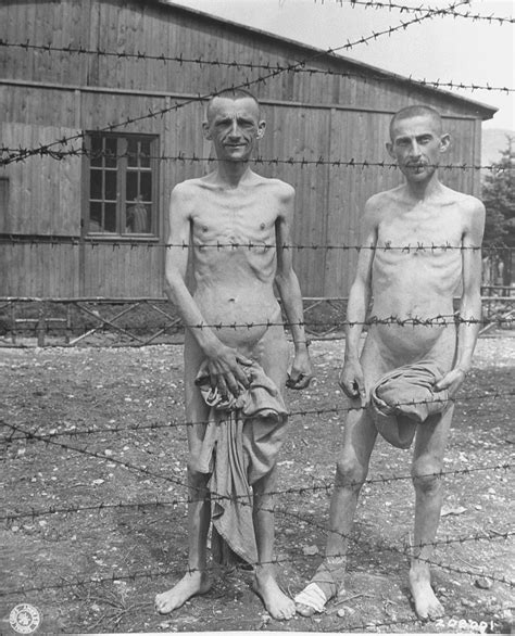 two emaciated survivors stand behind a barbed wire fence in the