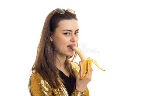 Pretty Young In Golden Jacket Looking At The Camera And Eating A Banana