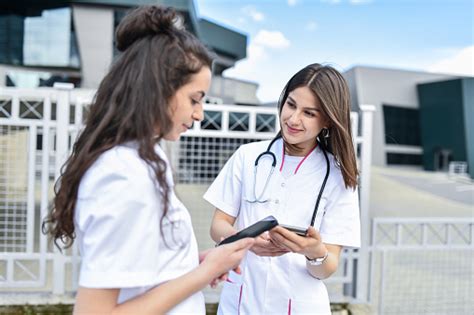 two cute nurses taking work break to use digital wallets on smartphones