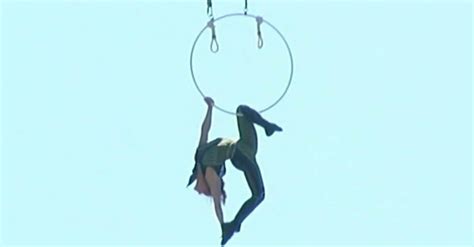 woman hangs upside down from a helicopter above racetrack as if it s