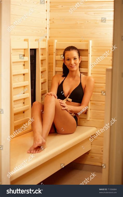 pretty woman wearing bikini sitting in sauna smiling at