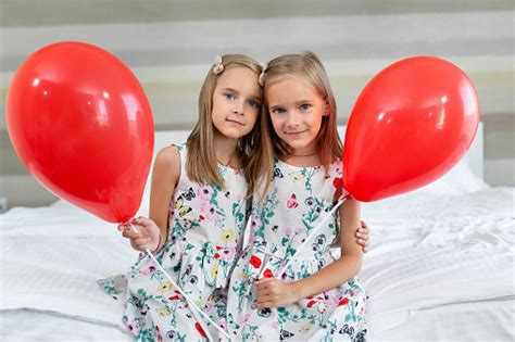 two twin sisters in beautiful dresses are sitting on a bed in a hotel