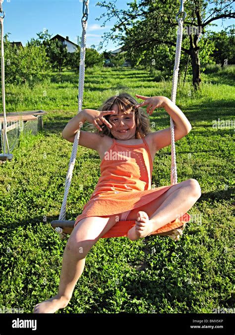4 year old german girl in orange dress playing on an outdoor swing