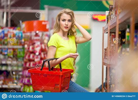 Beautiful Young Woman With Red Empty Shopping Cart In The Store Chooses