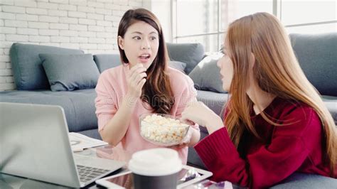 Lesbian Asian Couple Watching Tv Laugh And Eating Popcorn In Living